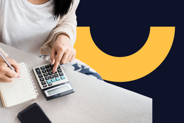 Person writing in a notebook and using a calculator, with a mobile phone placed next to it