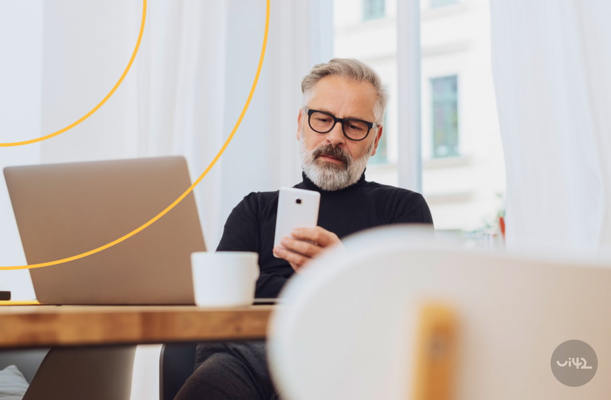 A man sitting at a table with a laptop and a mobile phone in his hand.