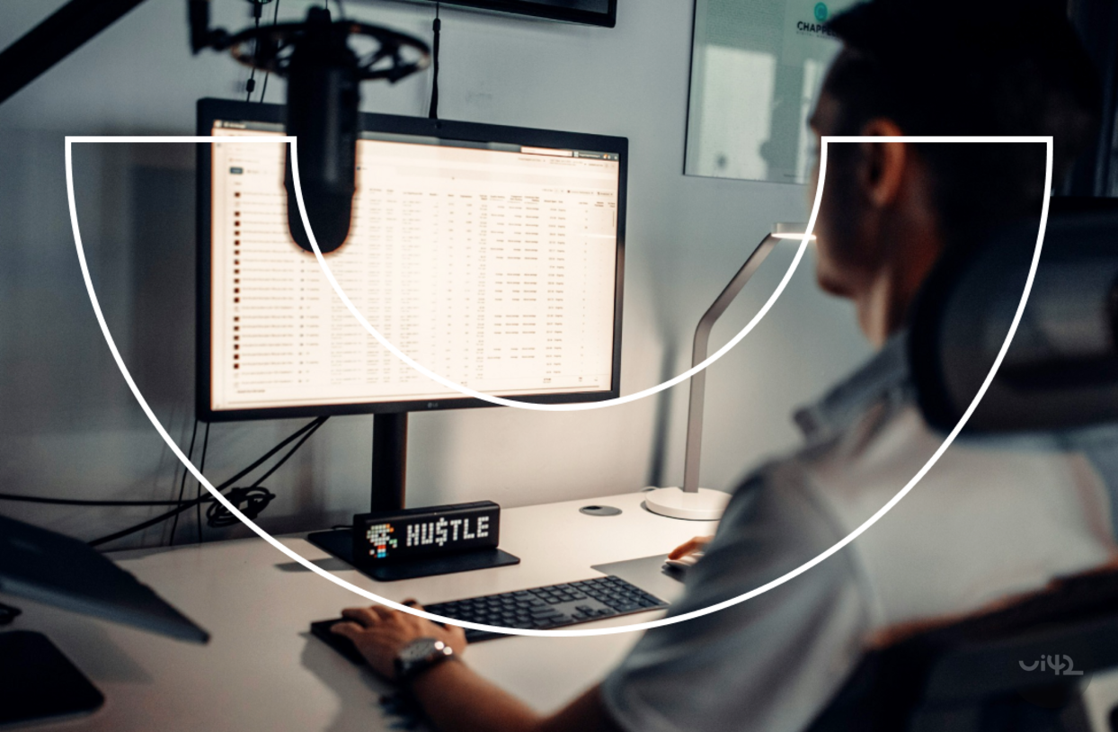A person working on a computer with a large monitor displaying tables, in an office environment with modern equipment.