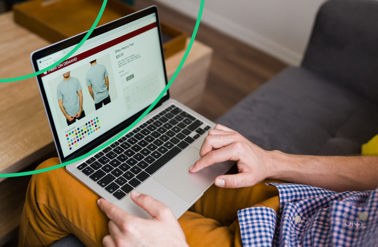 A person shopping for clothes online on a laptop, a webpage is displayed with a t-shirt and color options.