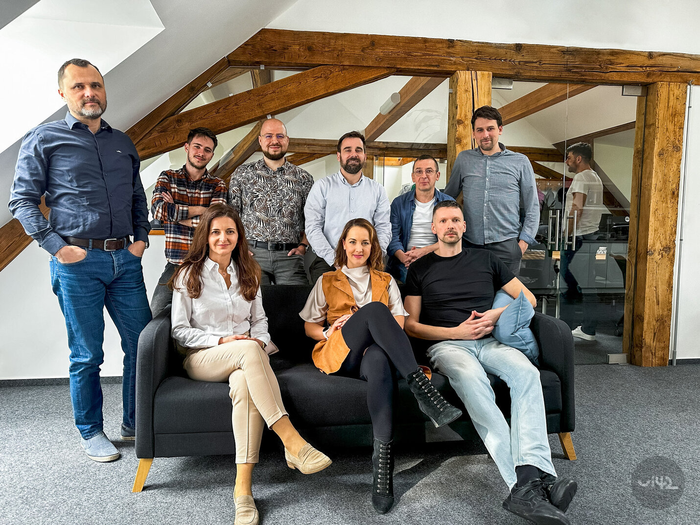 Group photo of people in an office, sitting and standing around a couch.