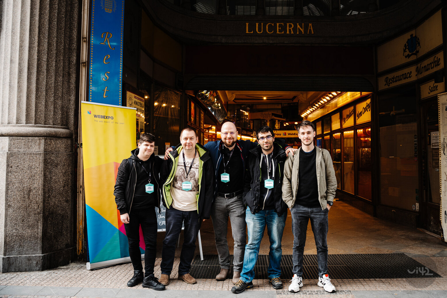 A group of people in front of a building with the sign Lucerna and a WebExpo banner, likely web developers or conference attendees.